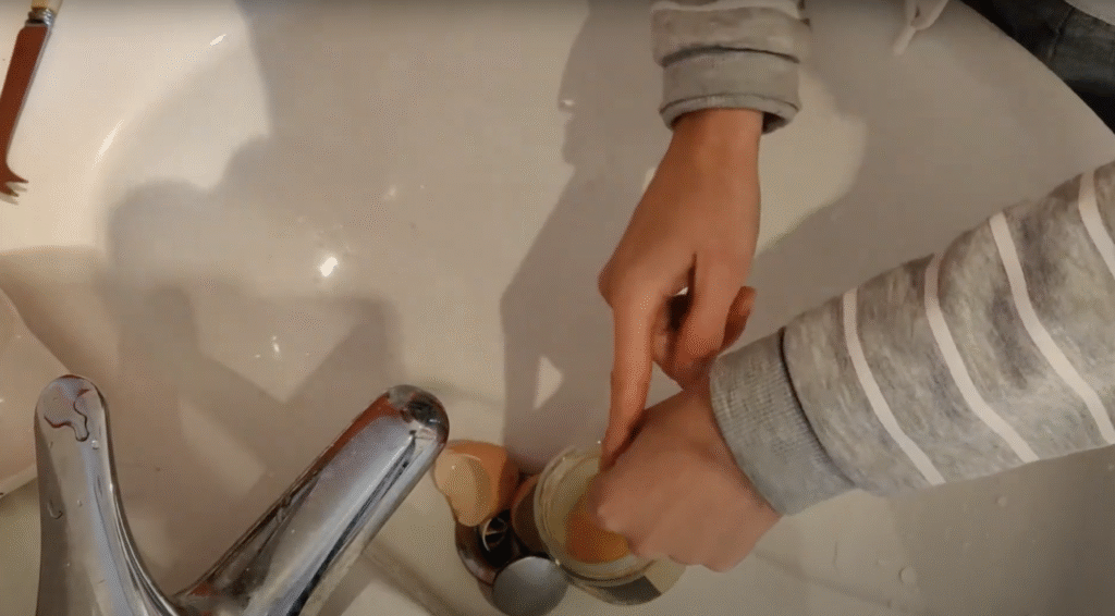 Seen from above, a pair of hands gently squeeze an egg yolk into a glass jar that sits in a sink.